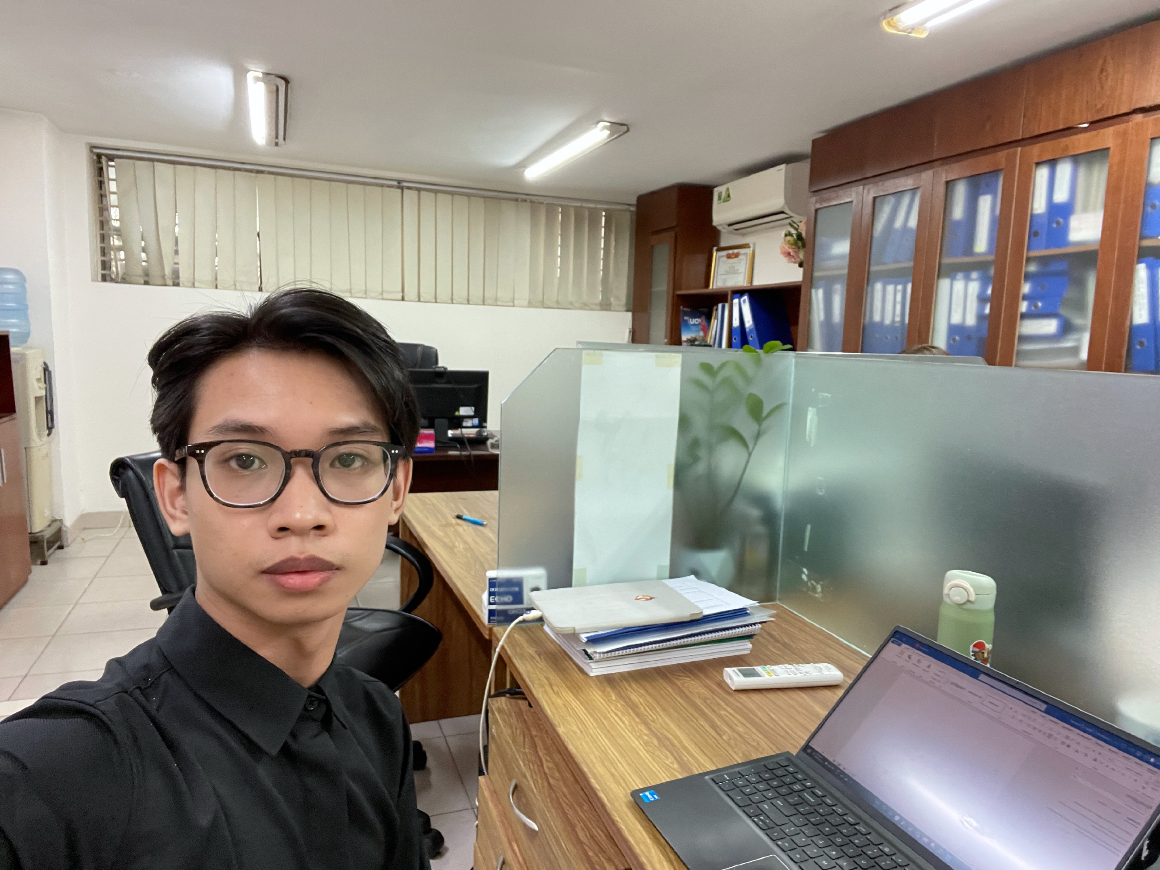 James sitting at his office desk looking frustrated, unable to check his phone for trading alerts while his manager is nearby